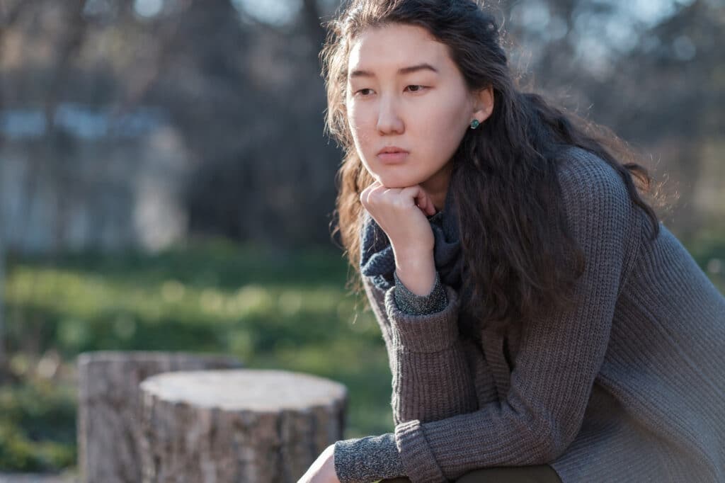 Young woman sitting outdoors in thoughtful reflection, representing self-awareness, emotional healing, and personal growth during recovery.
